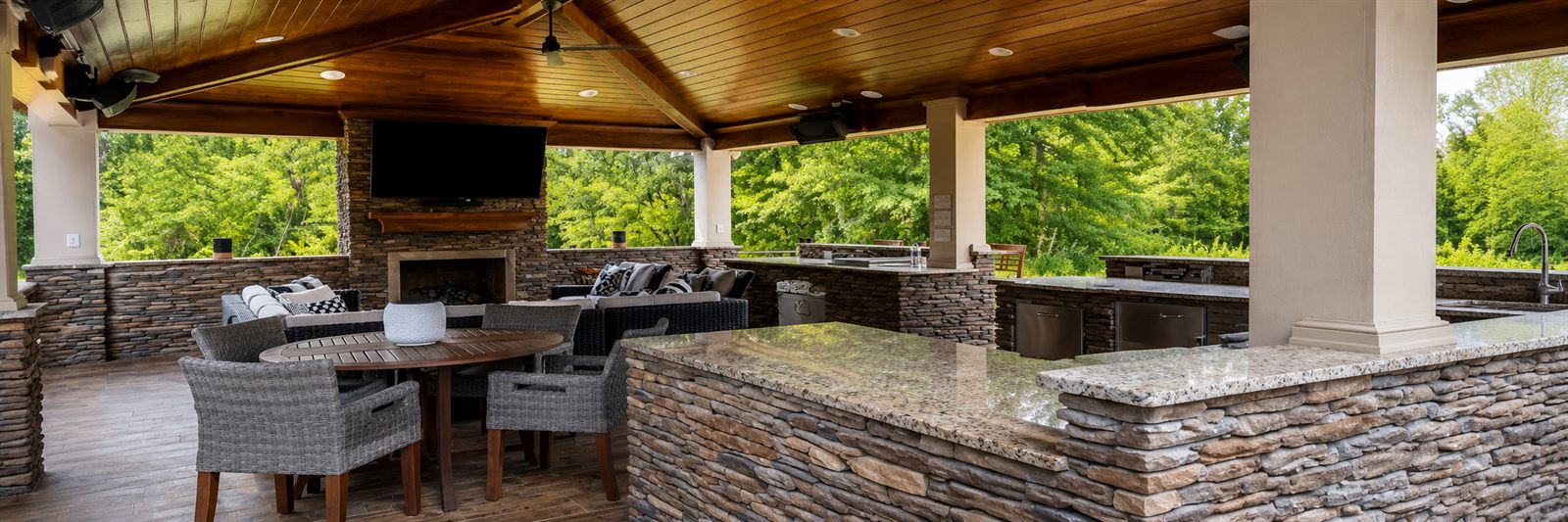 Outdoor living pavilion with wood ceiling and stone bar, built by Custom Services